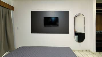Quarto com cama, televisão na parede, espelho e guarda-roupa.