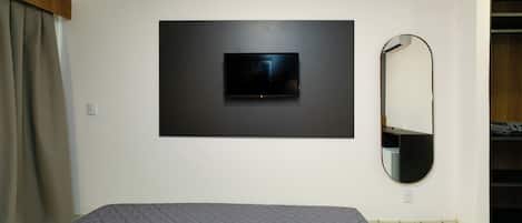 A bedroom with a bed, a mounted TV, a mirror, and a wardrobe.