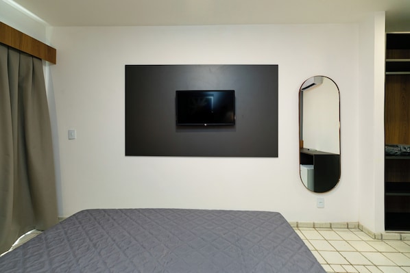 A bedroom with a bed, a mounted TV, a mirror, and a wardrobe. - El Aram Beach Cabo All Inclusive (Cabo de Santo Agostinho)