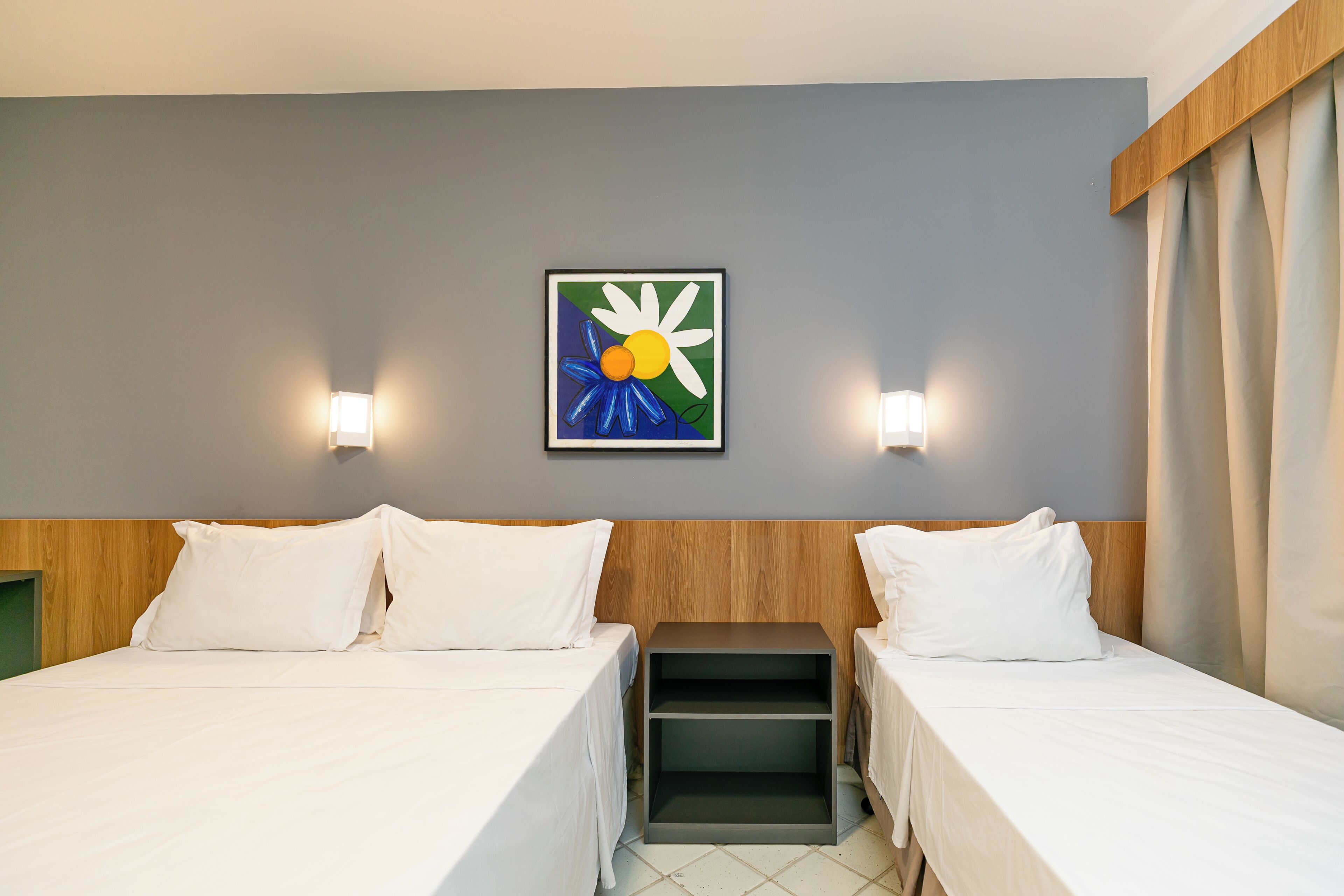 Habitación de hotel con dos camas, una mesita de noche, una pequeña mesa y una obra de arte enmarcada en la pared.