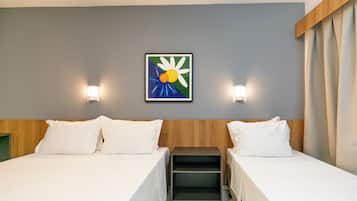 Habitación de hotel con dos camas, una mesita de noche, una pequeña mesa y una obra de arte enmarcada en la pared.