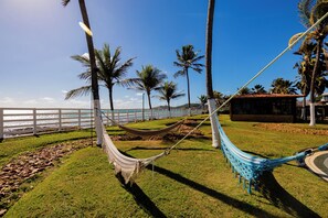 A hammock between palm trees, a white fence, and a building with a tiled roof. - El Aram Beach Cabo All Inclusive (Cabo de Santo Agostinho)