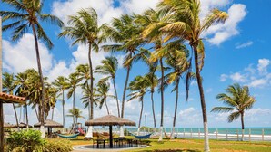 A tropical resort with palm trees, a beach, and a thatched-roof pavilion. - El Aram Beach Cabo All Inclusive (Cabo de Santo Agostinho)