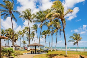 A tropical resort with palm trees, a beach, and a thatched-roof pavilion. - El Aram Beach Cabo All Inclusive (Cabo de Santo Agostinho)