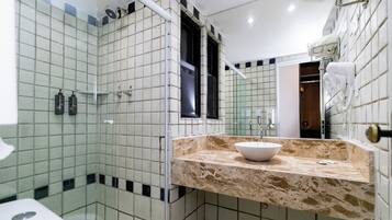 Casa de banho com cabine de chuveiro de vidro, pia com bancada de mármore e espelho.