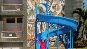 A swimming pool with a blue slide and a mural of sea creatures on the adjacent building. - El Aram Beach Cabo All Inclusive (Cabo de Santo Agostinho)