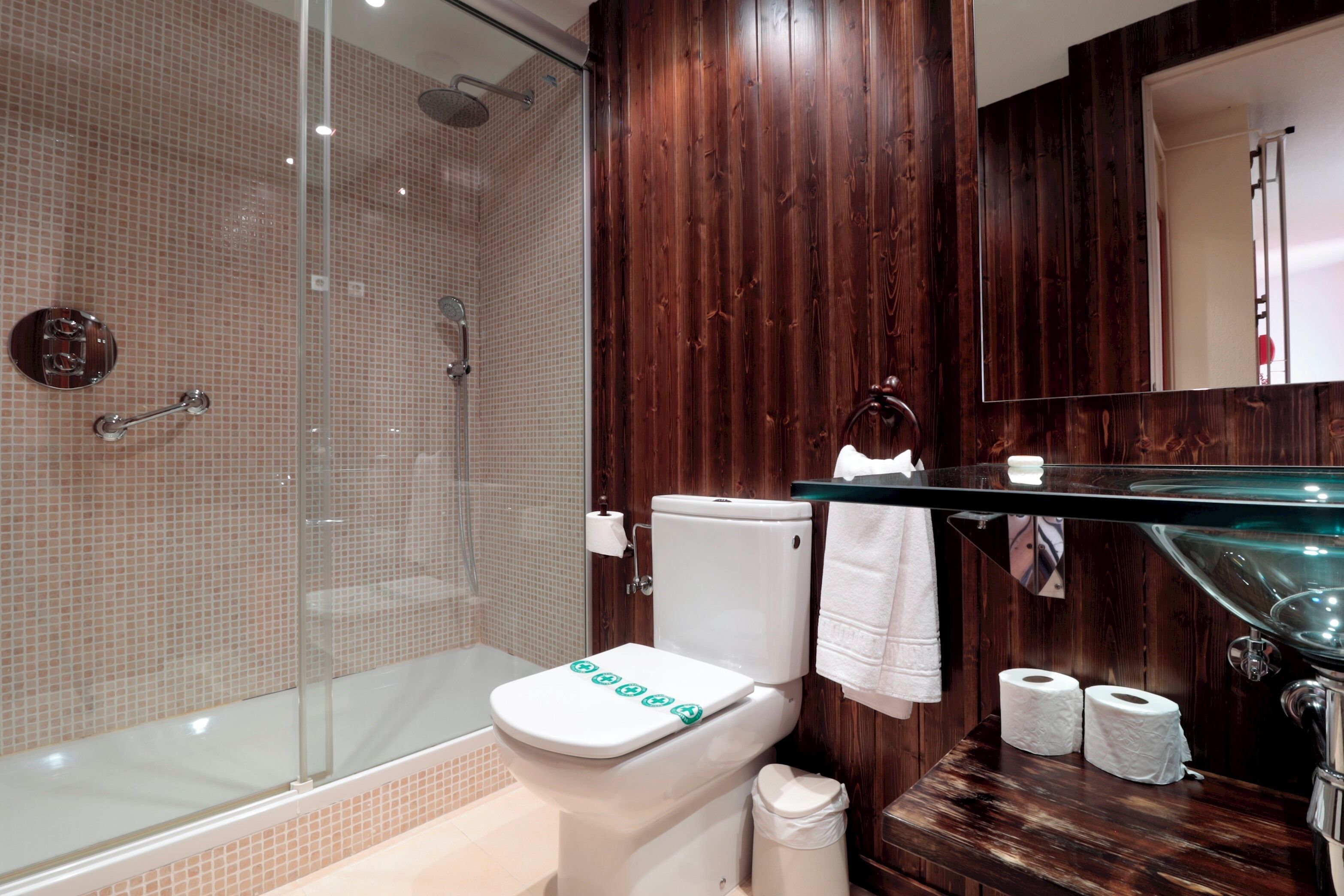 A modern bathroom with a glass shower enclosure, a white toilet, and a wooden vanity with a glass sink.