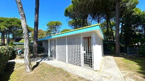 A small, enclosed outdoor structure with a blue roof and white walls, surrounded by trees and a paved path. - VILLA NORTH 321B - A2 6+0 - B03215 (Bibione Pineda)