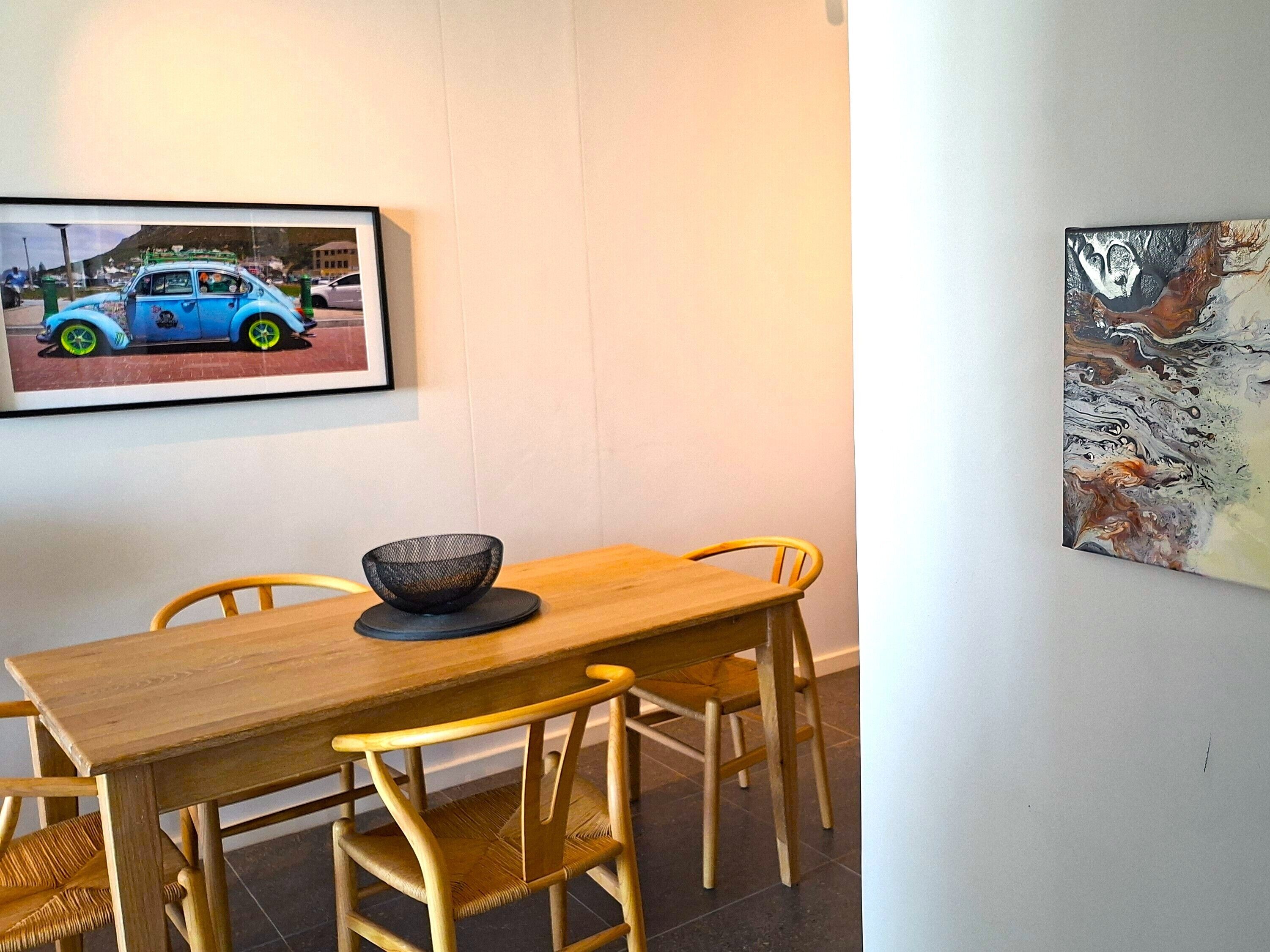 A dining area with a wooden table and chairs, a black bowl on the table, and two framed pictures on the wall.