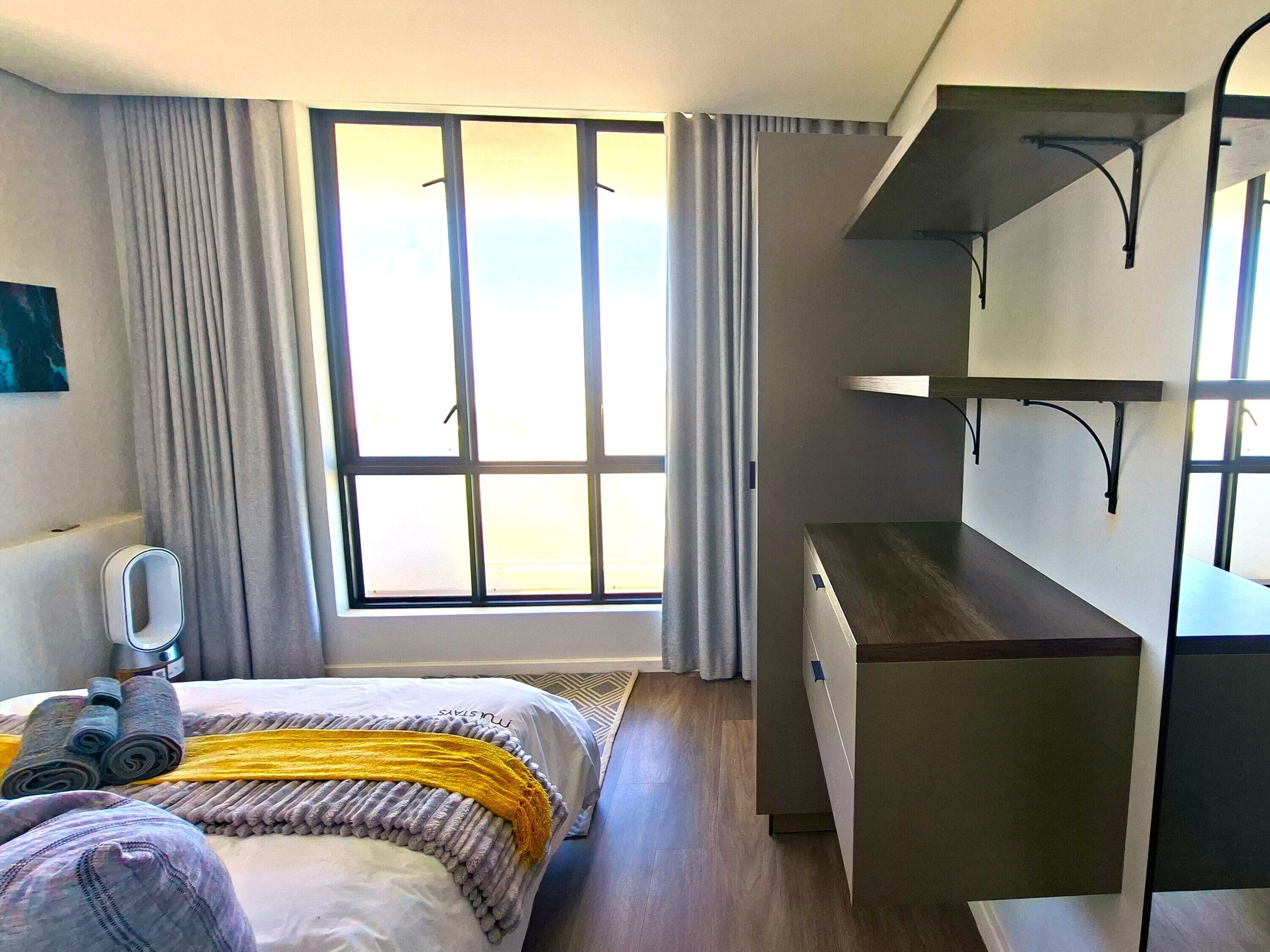 A hotel room with a bed, a desk, a chair, a mirror, and a window with curtains.
