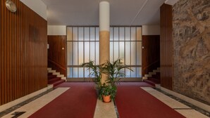 Un pasillo con alfombra roja, paneles de madera, una columna central y una planta en maceta.