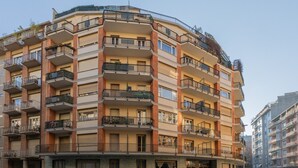 Un edificio residencial de varios pisos con balcones, entrada al nivel del suelo y un área de estacionamiento visible.