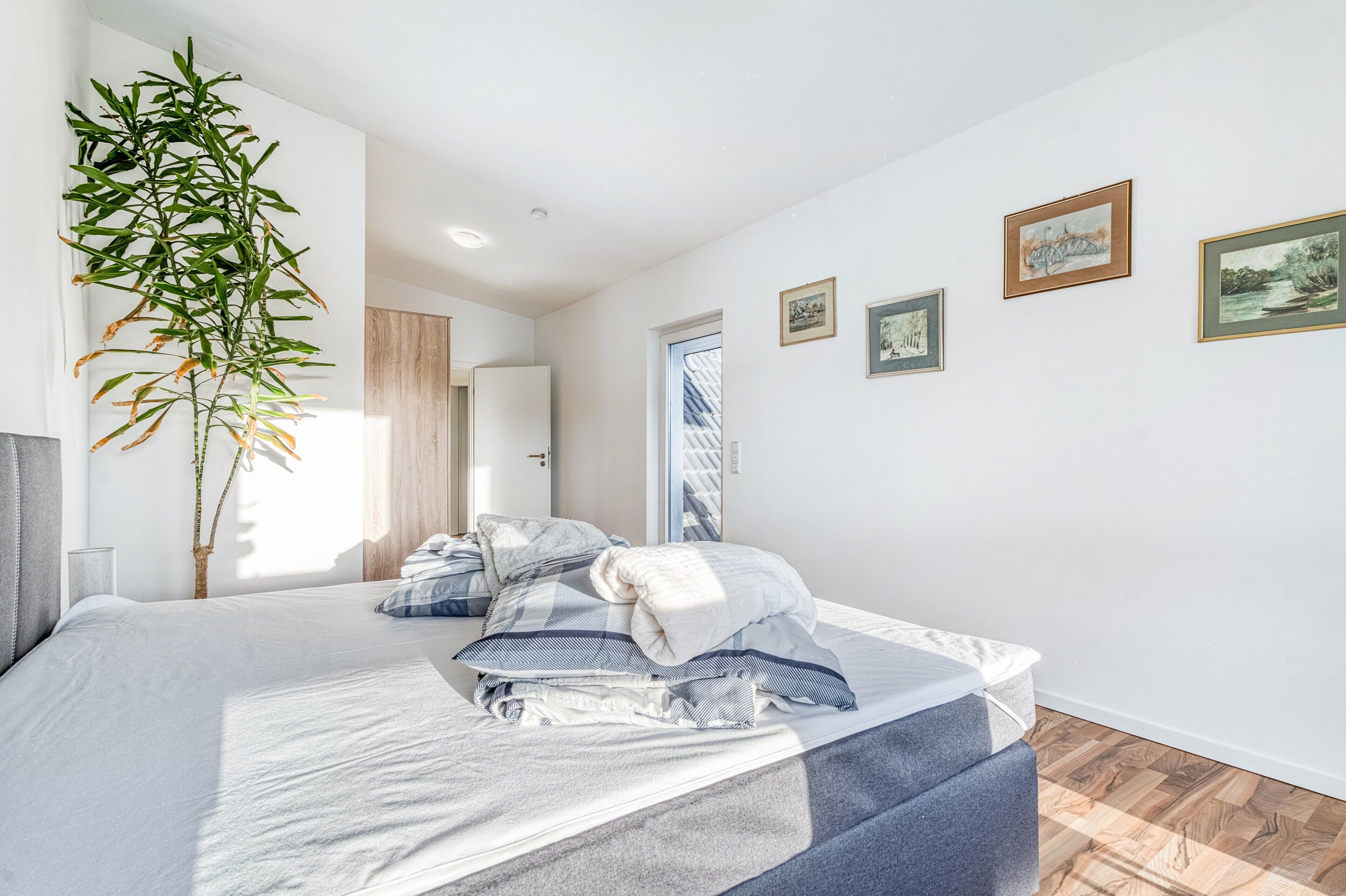 Een moderne slaapkamer met een groot bed, een kamerplant en kunstwerken in een lijst aan de muur.