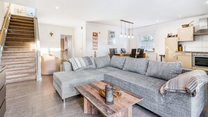 A modern living room with a grey sectional sofa, a wooden coffee table, and a staircase leading to another level. - Holiday Home 'Haus Primavera' with Shared Terrace, Private Garden and Wi-Fi (Bad Bentheim)