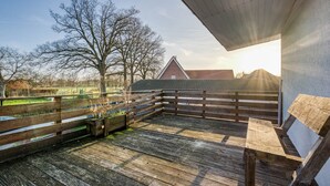 A wooden deck with benches, a fenced area, and a view of a building with a red roof. - Holiday Home 'Haus Primavera' with Shared Terrace, Private Garden and Wi-Fi (Bad Bentheim)
