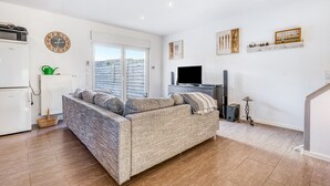 A living room with a sofa, a television, a radiator, a clock, and a window with blinds. - Holiday Home 'Haus Primavera' with Shared Terrace, Private Garden and Wi-Fi (Bad Bentheim)