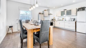 A modern kitchen with white cabinets, a wooden dining table, and black chairs. - Holiday Home 'Haus Primavera' with Shared Terrace, Private Garden and Wi-Fi (Bad Bentheim)