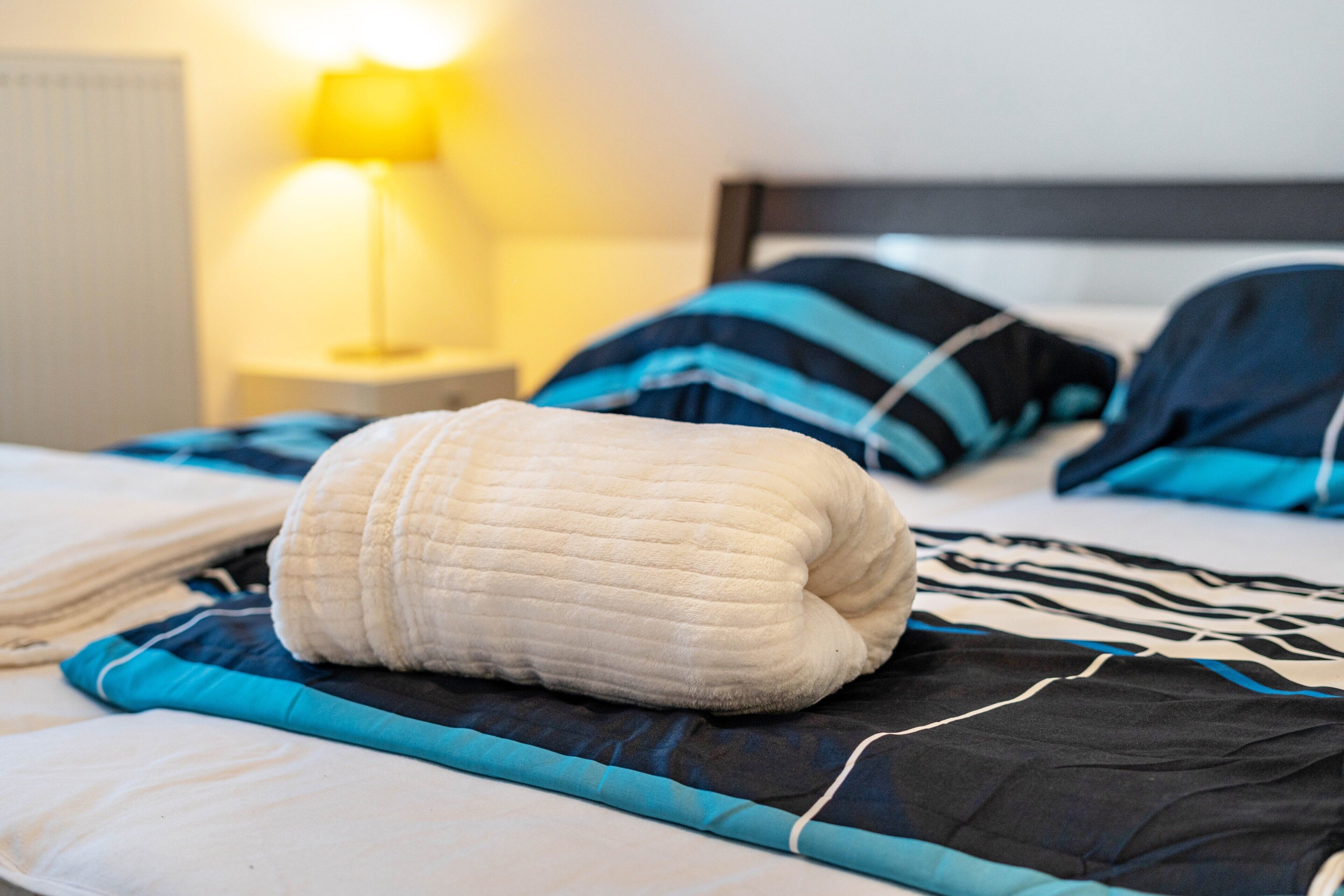 Ein Bett mit einem weißen Kopfkissen, einer blau-schwarz gestreiften Decke und einer Nachttischlampe.
