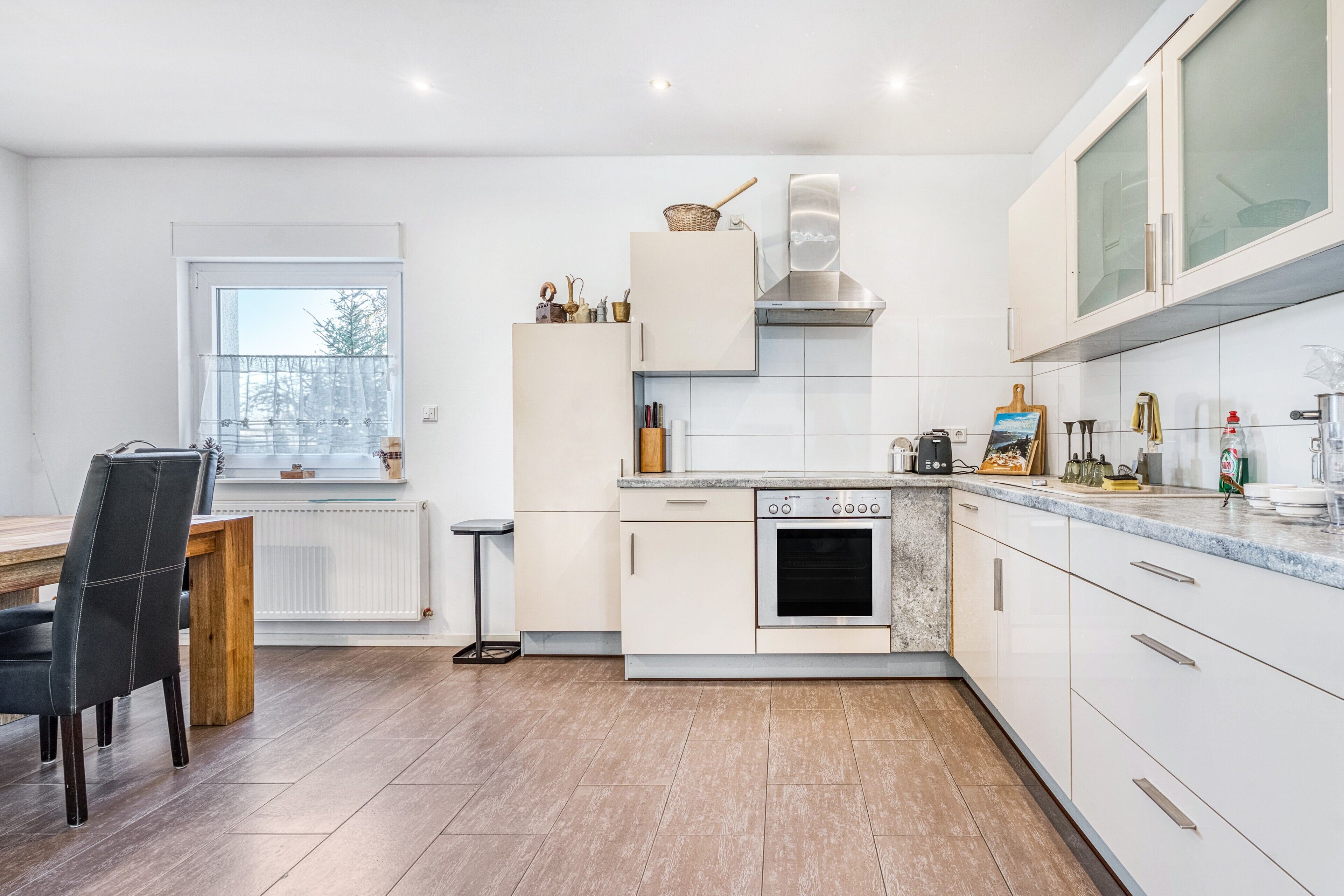A modern kitchen with white cabinets, a built-in oven, and a dining area with a wooden table and chairs.