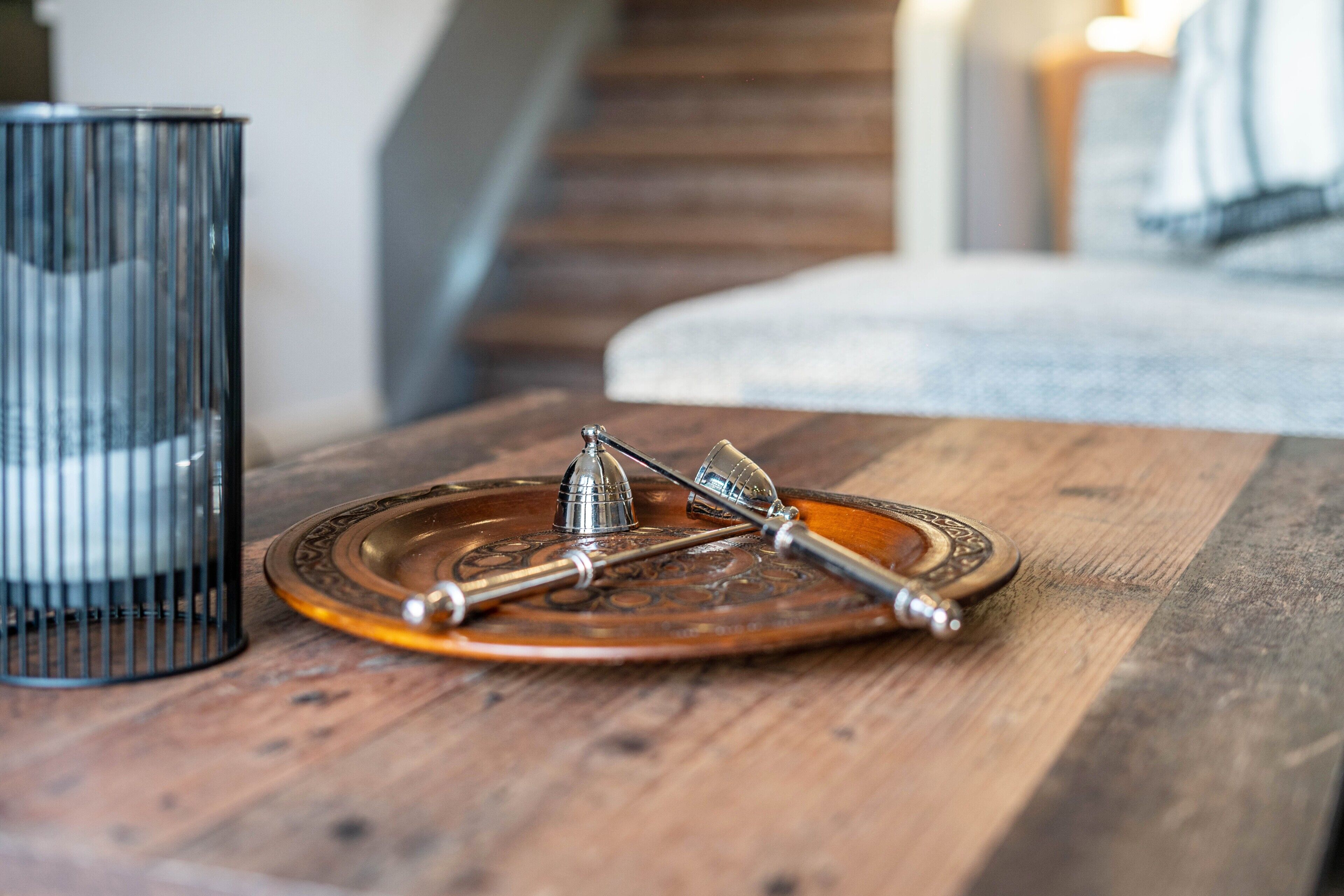 A wooden table with a decorative plate and two metal objects, possibly a compass and a candle holder, and a black metal candle holder in the background.