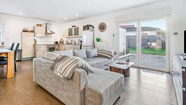 A modern living room with a sofa, a coffee table, and a kitchen area with cabinets and a refrigerator. - Holiday Home 'Haus Primavera' with Shared Terrace, Private Garden and Wi-Fi (Bad Bentheim)