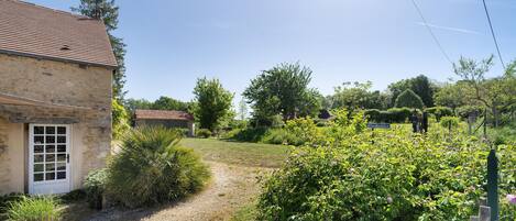 A stone building with a tiled roof, a gravel path, and lush greenery.