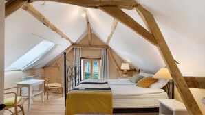 Un dormitorio con techo inclinado, una cama, una silla, una mesa y un ventanal.