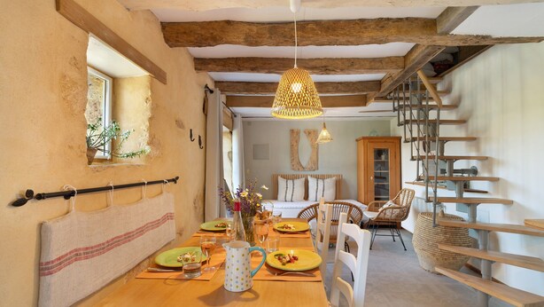 Un comedor con una mesa de madera, sillas, una lámpara colgante y una escalera.