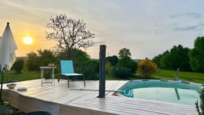 Um deck de madeira com piscina, uma cadeira e uma mesa com chapéu.