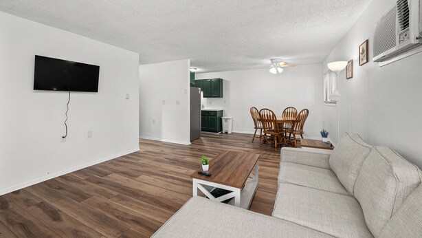 A modern living room with a flat-screen TV, wooden flooring, a gray sofa, and a dining area with a table and chairs. - Enjoyable 1-bedroom apartment with AC in charming Le Claire (Le Claire)