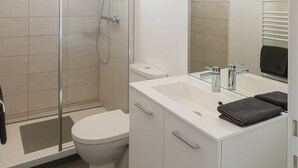 A modern bathroom with a glass-enclosed shower, a white toilet, and a vanity with a mirror.