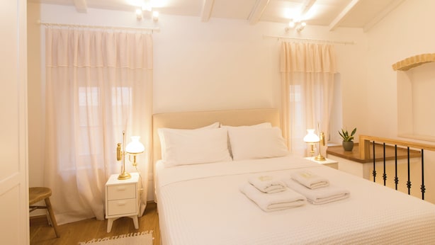 A neatly arranged bedroom with a large bed, two bedside tables with lamps, a wooden bench, and a potted plant. - Il Sogno by Corfuescapes  (Corfu)