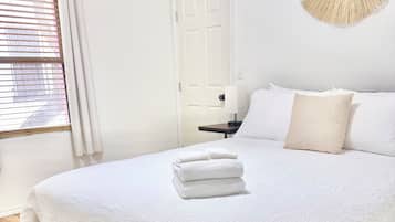 A neatly made bed with a white duvet, a bedside table with a lamp, and a door in the background.
