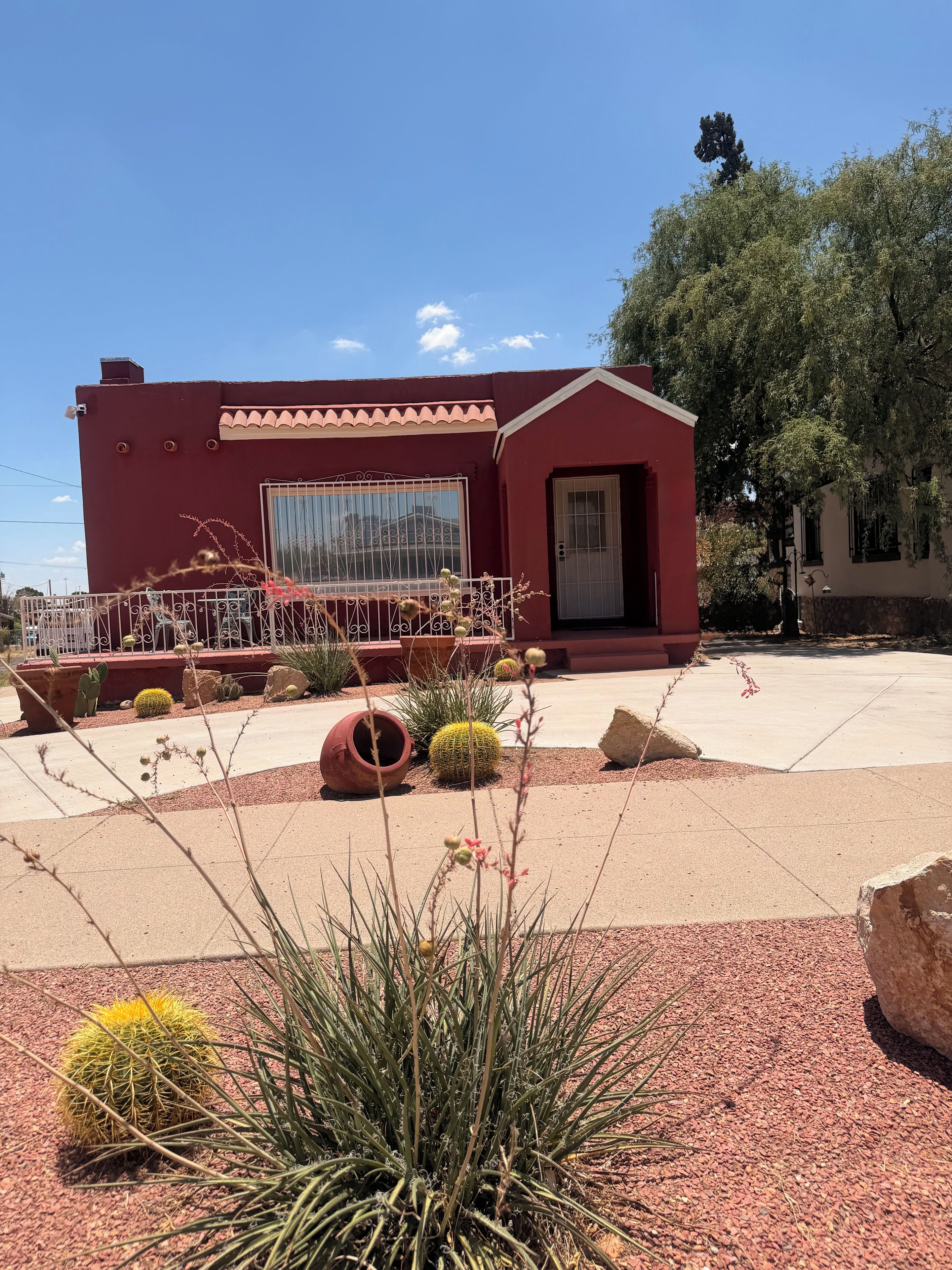 A building with a red exterior, a large window, and a door. There are cacti and desert plants in the foreground.