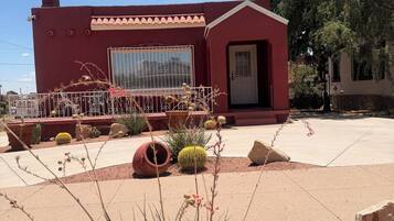 A building with a red exterior, a large window, and a door. There are cacti and desert plants in the foreground.
