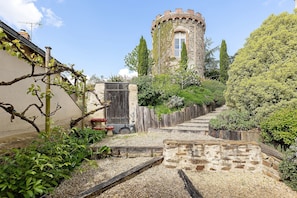A stone tower with a window, surrounded by greenery and a gravel path.