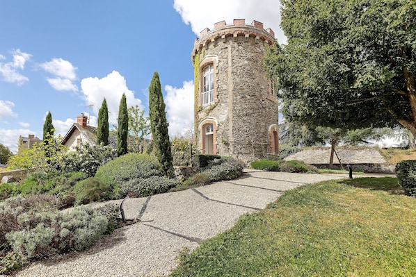 A stone tower with a circular design, surrounded by a gravel path and various shrubs.