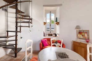 A spiral staircase, a round dining table, a sofa with cushions, a wooden cabinet, and a window with a view.