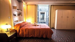 Ein Hotelzimmer mit einem Bett, einem Schreibtisch mit Lampe, einem Kleiderschrank und einem gemusterten Boden.