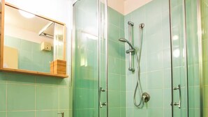 Ein Badezimmer mit einer Duschkabine, einem Waschbecken mit Spiegel und einer Holzkommode.