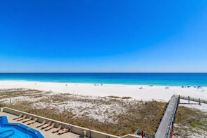 Blick auf einen Strand mit Poolbereich, einer Holzterrasse und blauem Himmel.