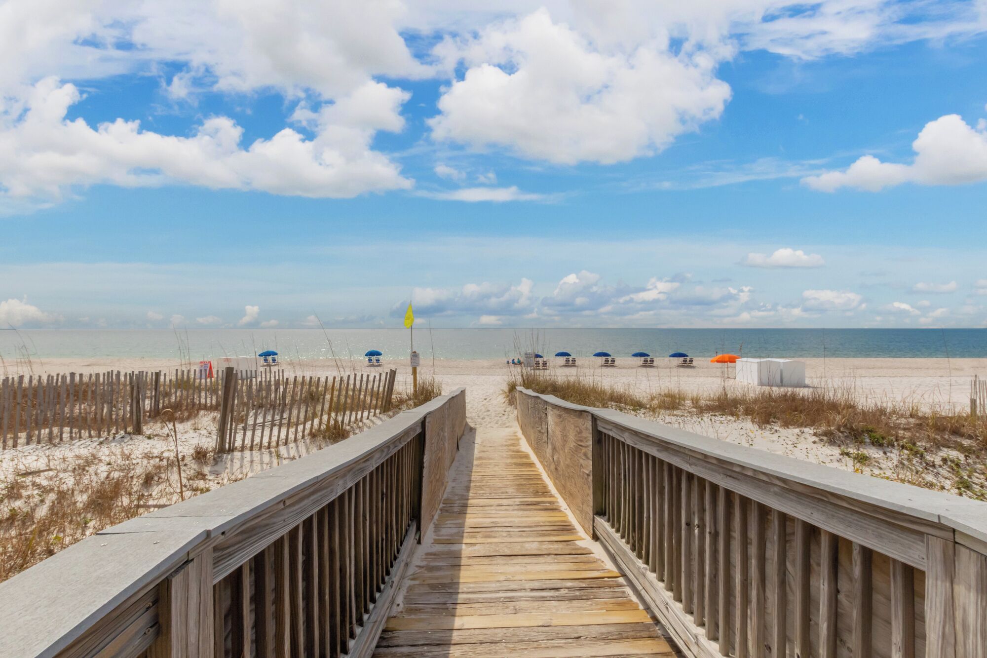 A wooden boardwalk leading to a beach with umbrellas and beach chairs.