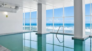 Une piscine intérieure offrant une vue dégagée sur l’océan grâce à de grandes baies vitrées.