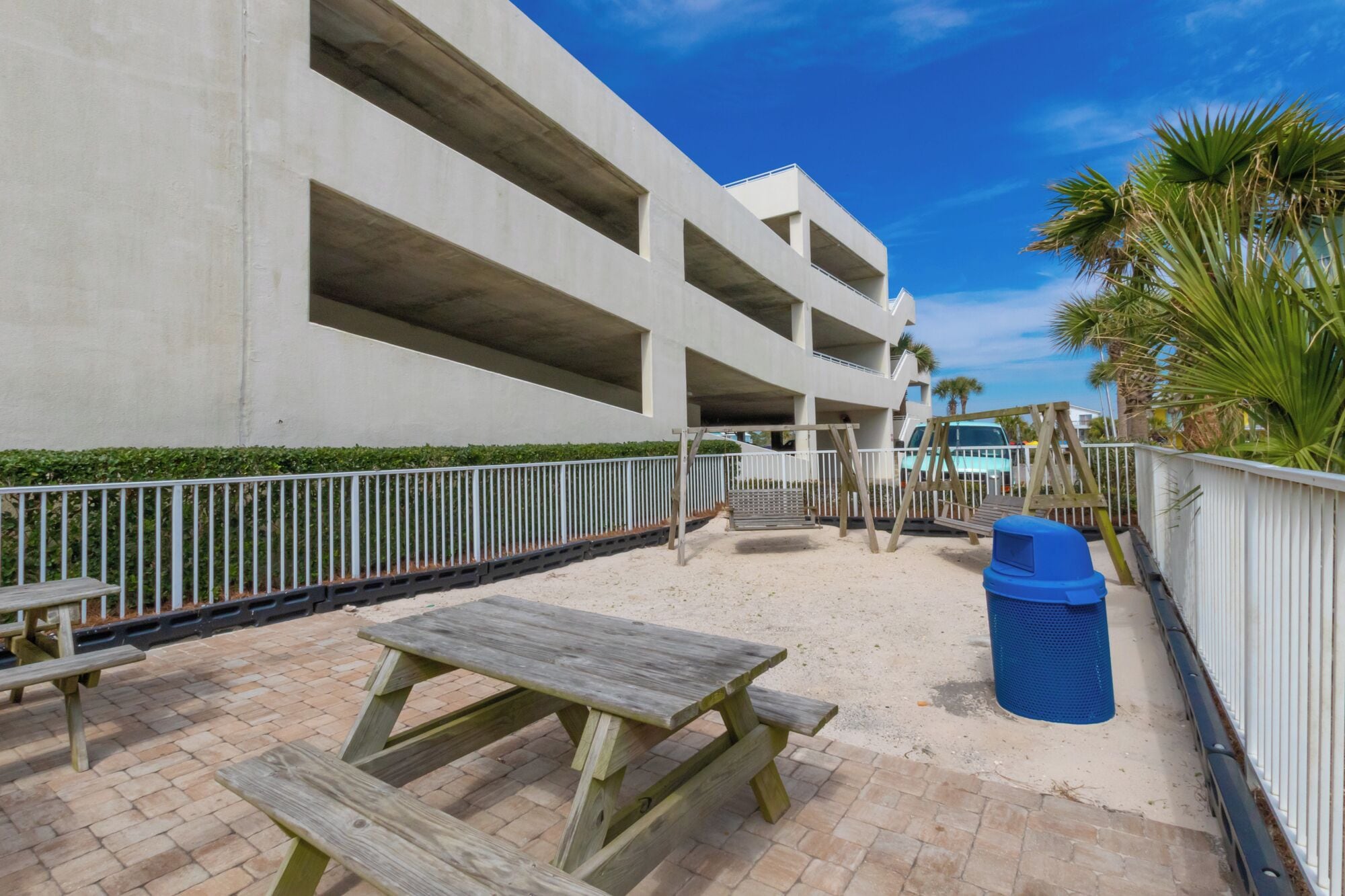 A beachside parking structure with multiple levels, a picnic table, and a trash bin.
