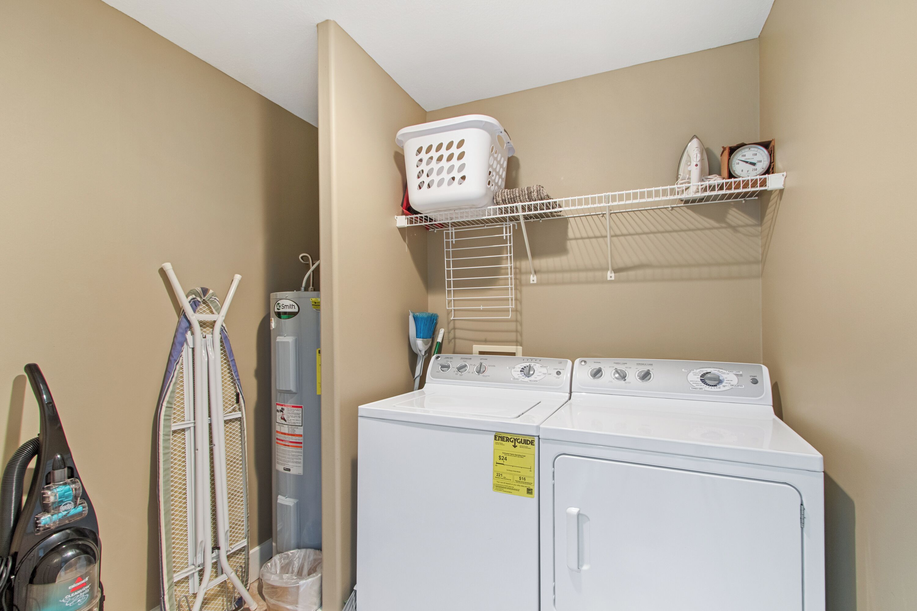 A laundry area with a washing machine, a dryer, a vacuum cleaner, and a shelf with a basket and a clock.