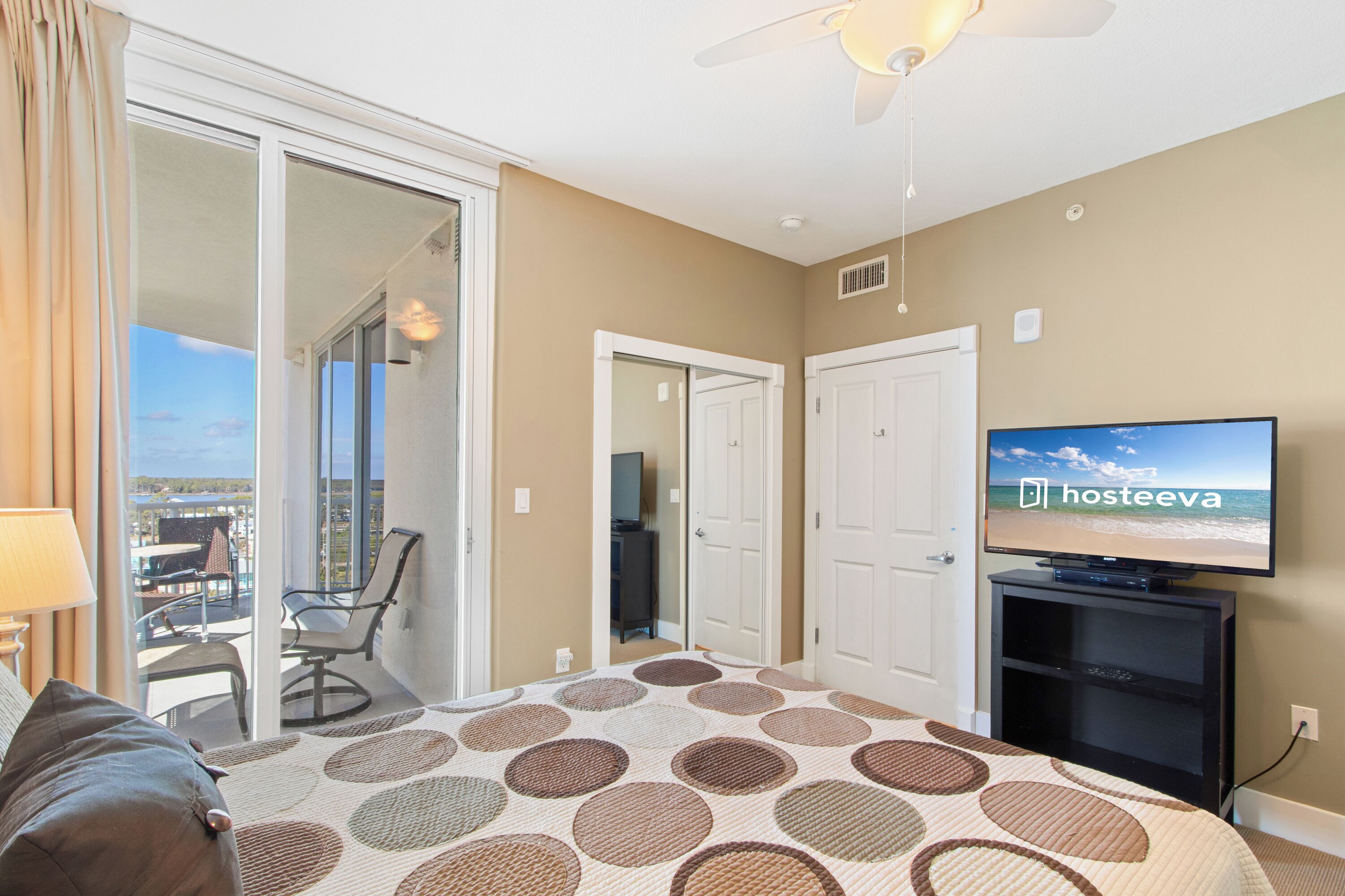 A hotel room with a large bed, a television, a balcony with a chair, and a view of the beach.