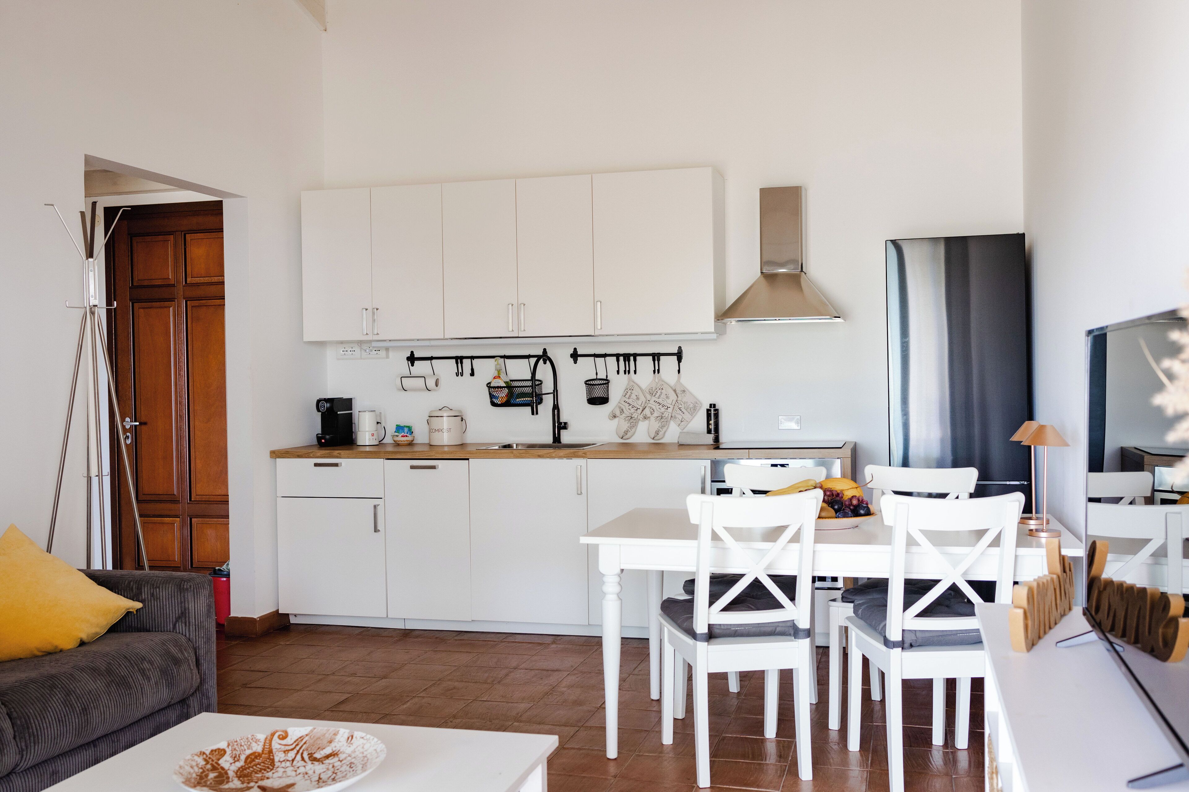 A compact kitchen with white cabinets, a dining table with chairs, and a coffee machine.