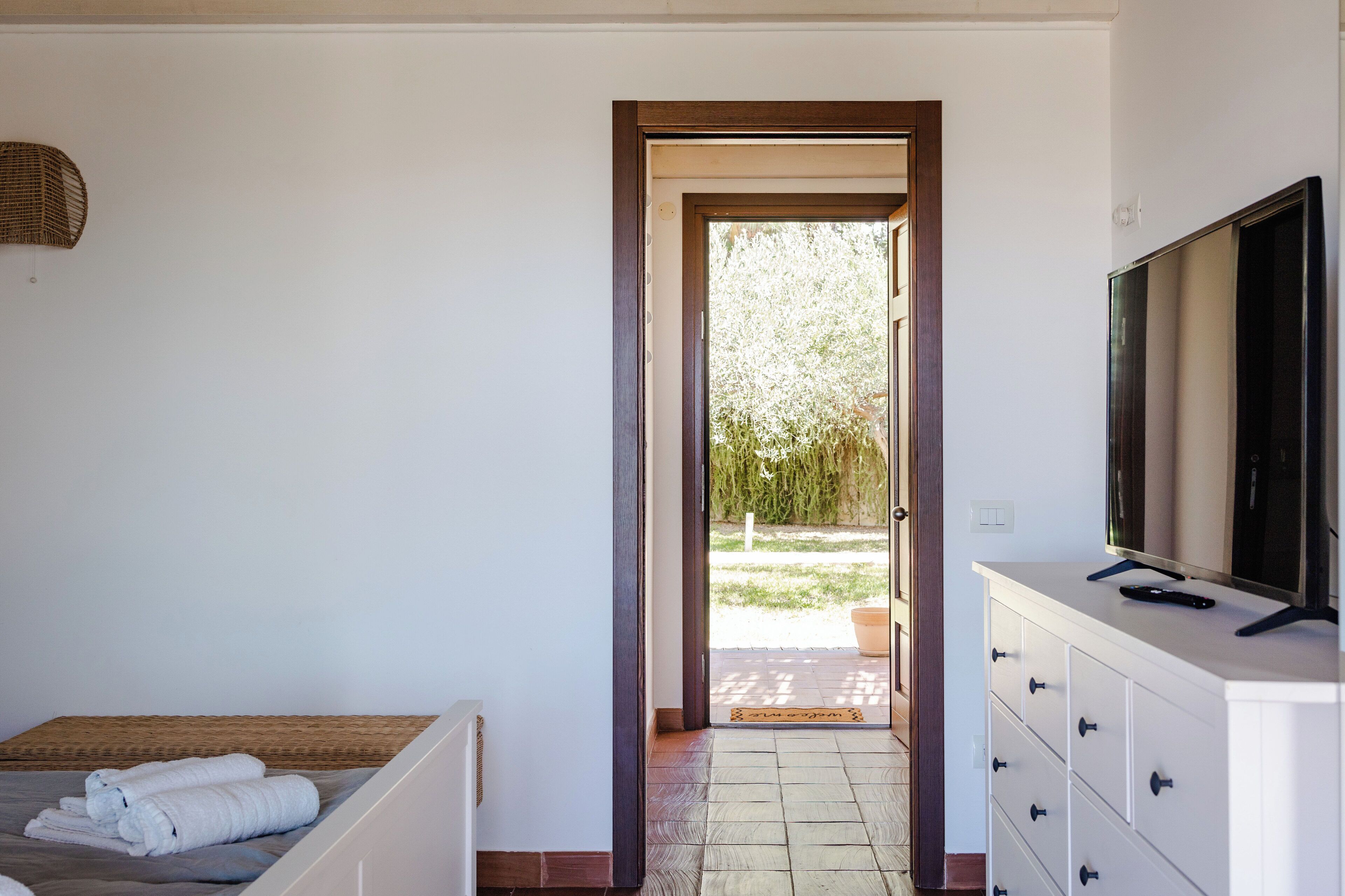 A bedroom with a bed, a TV on a dresser, and a door leading to an outdoor area with a garden.