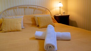 Ein ordentlich bezogenes Bett mit einem aufgerollten weißen Handtuch in der Mitte, zwei Kissen und einer Nachttischlampe auf einem Nachttisch.
