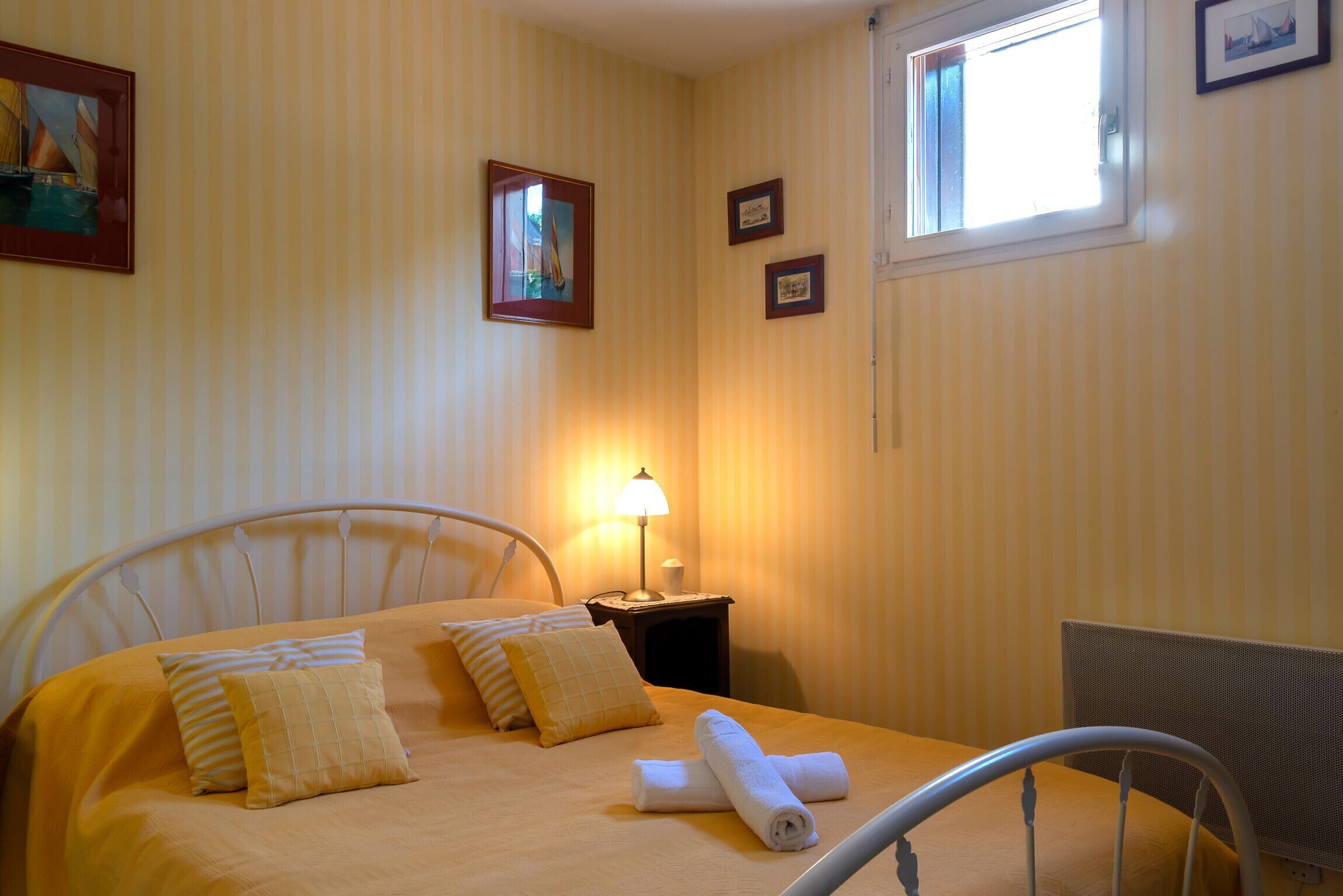 Un lit bien fait, avec une couvre-lit jaune et des oreillers, une lampe de chevet et une fenêtre donnant sur l’extérieur.